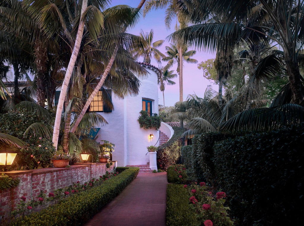 Spanish colonial-style luxury beachfront hotel with white stucco walls, red tile roofs, and manicured palm gardens overlooking the Pacific Ocean