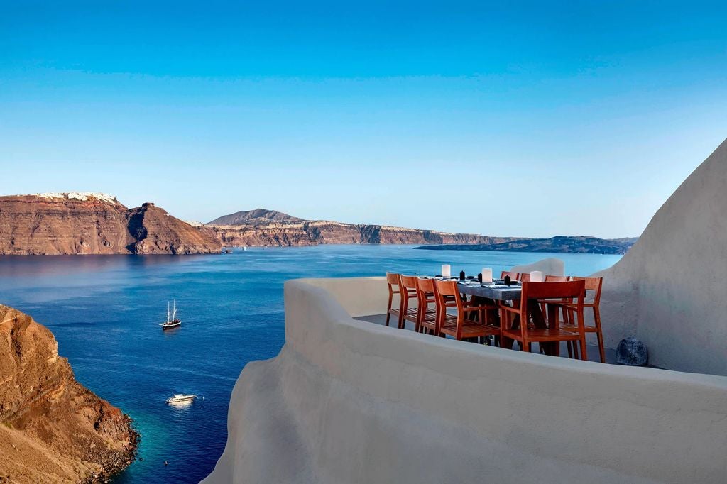 Cascading white-washed buildings with infinity pools perched on Santorini cliffs, overlooking turquoise Aegean Sea and volcanic caldera