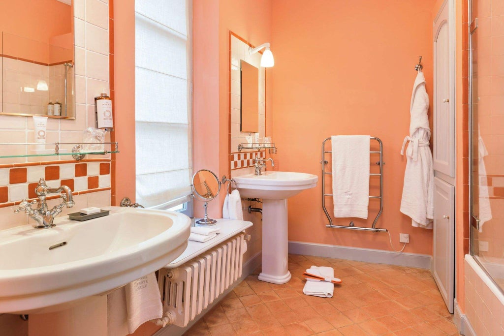 Elegant stone-walled hotel room with refined French countryside decor, soft linens, antique furnishings, and warm natural light filtering through vintage windows