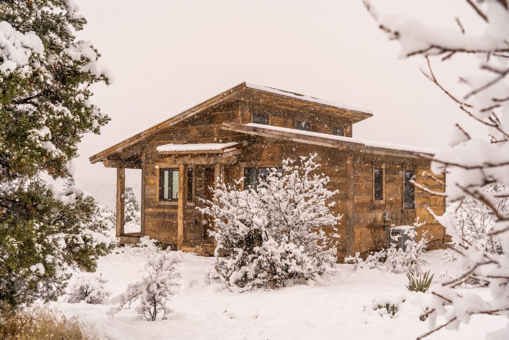 Rustic wooden lodge room with plush king bed, large windows overlooking scenic mountain landscape, warm earth-toned decor in scenic United States wilderness retreat