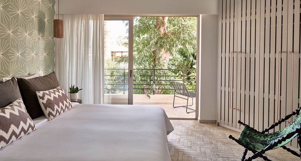 Spacious one-bedroom suite with elegant white and blue decor, wooden floor, plush bed, and panoramic balcony overlooking scenic Greek landscape at Phāea Cretan Malia resort