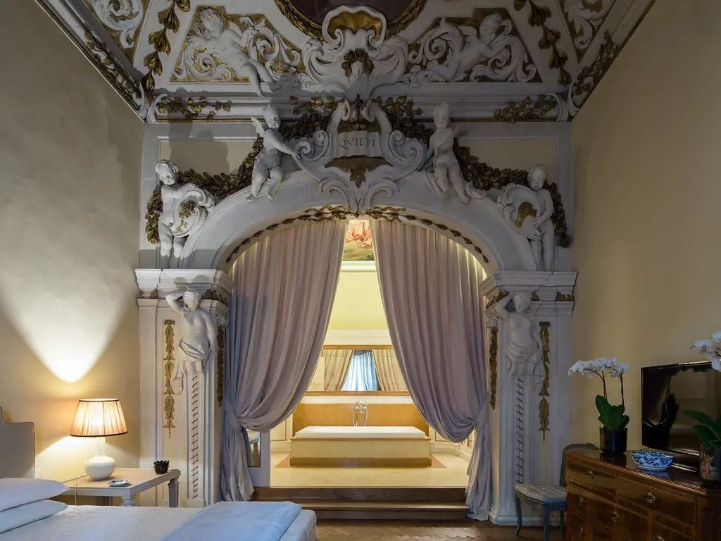 Elegant Italian junior suite with ornate ceiling, antique furnishings, rich velvet draperies, and ornamental chandelier in historic Palazzo di Camugliano