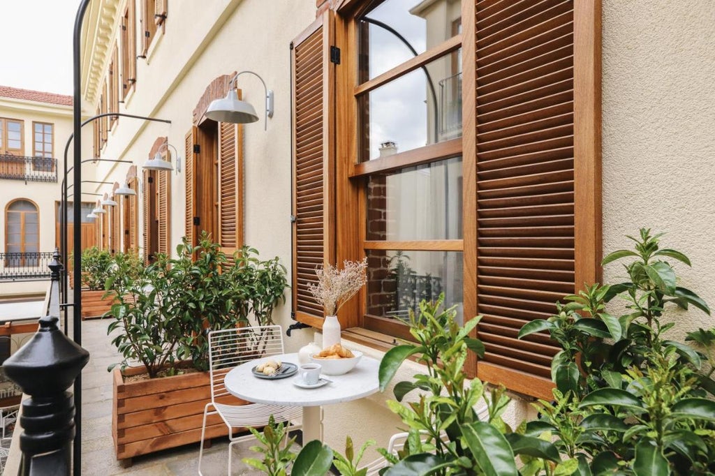 Historic stone hotel with elegant arched windows and balconies, surrounded by Mediterranean gardens and a sparkling pool in Turkey