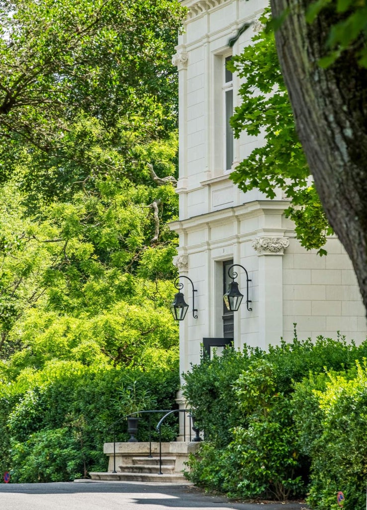 Elegant French château hotel with ivory stone walls, arched windows and climbing ivy, set against manicured gardens and mature trees