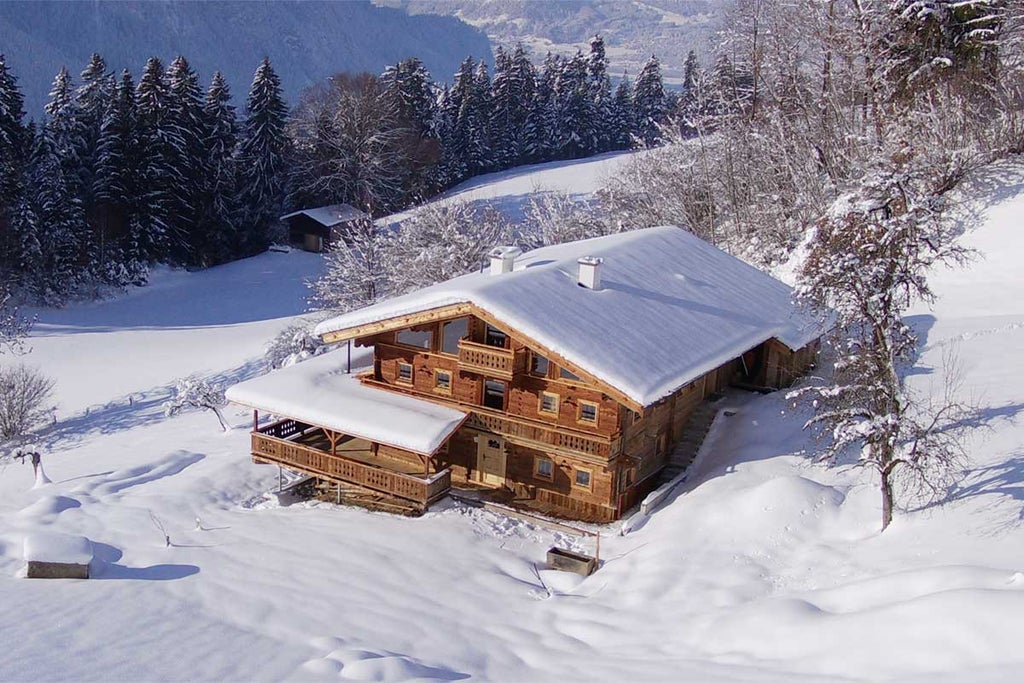 Traditional Austrian alpine hotel with wooden balconies and terraces overlooking snow-capped mountains, set against clear blue skies