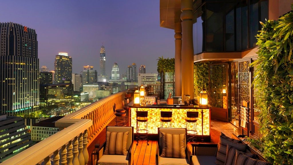 Dramatic aerial view of Bangkok's modern skyline at sunset, with glowing golden skyscrapers and the winding Chao Phraya river below