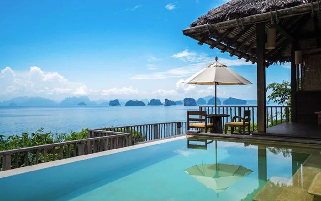 Luxurious infinity pool overlooking limestone cliffs and emerald waters of Phang Nga Bay, with teak sun loungers and tropical foliage