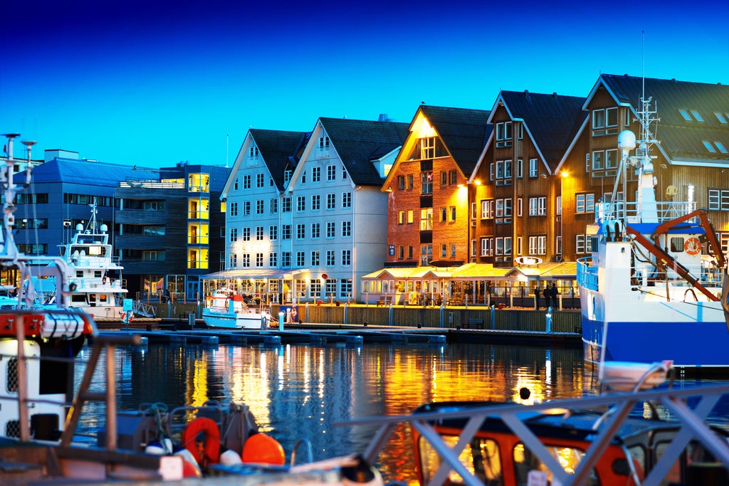 Mid-sized wooden fishing boats moored at snowy harbor with colorful Nordic buildings and snow-capped mountains rising behind Tromsø