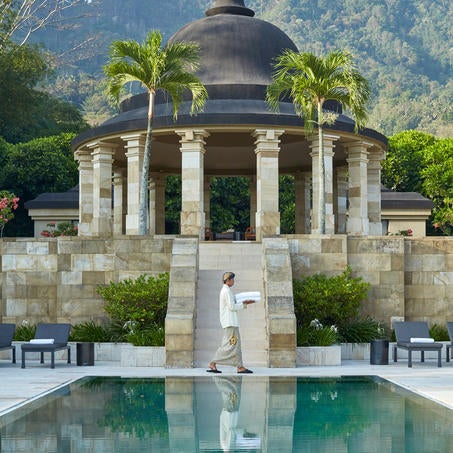 Luxury Indonesian resort with domed stone pavilions overlooking misty volcanic mountains, featuring serene infinity pool at sunrise