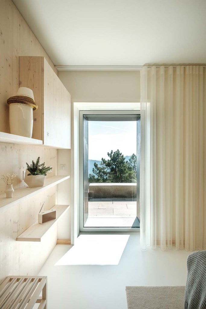 Elegant mountain-view hotel room with modern design, featuring minimalist wooden furniture, floor-to-ceiling windows, and luxurious white bedding in Portugal's scenic landscape