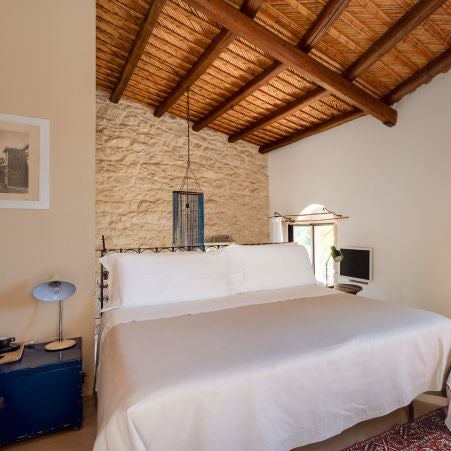 Rustic Mediterranean bedroom with stone walls, soft linen bedding, and warm terracotta tones at luxury boutique hotel in Sicilian countryside