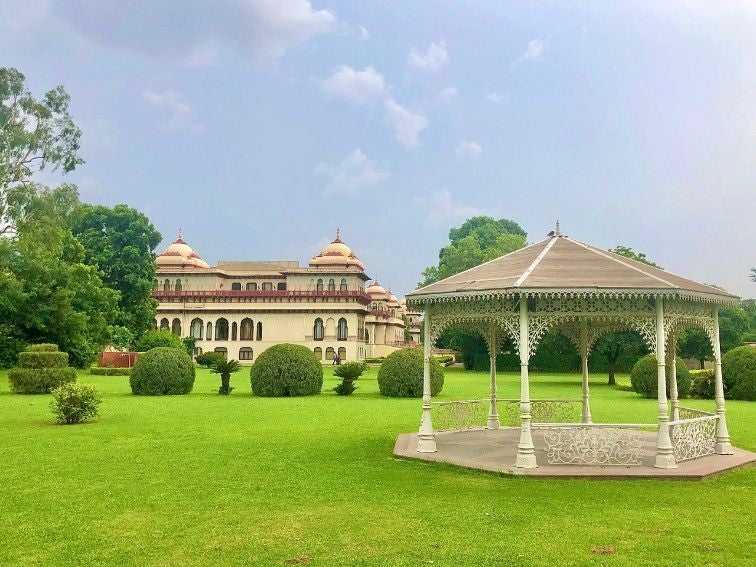 Majestic Rambagh Palace hotel in Jaipur features ornate sandstone archways, pristine gardens, and a grand domed entrance lit at dusk