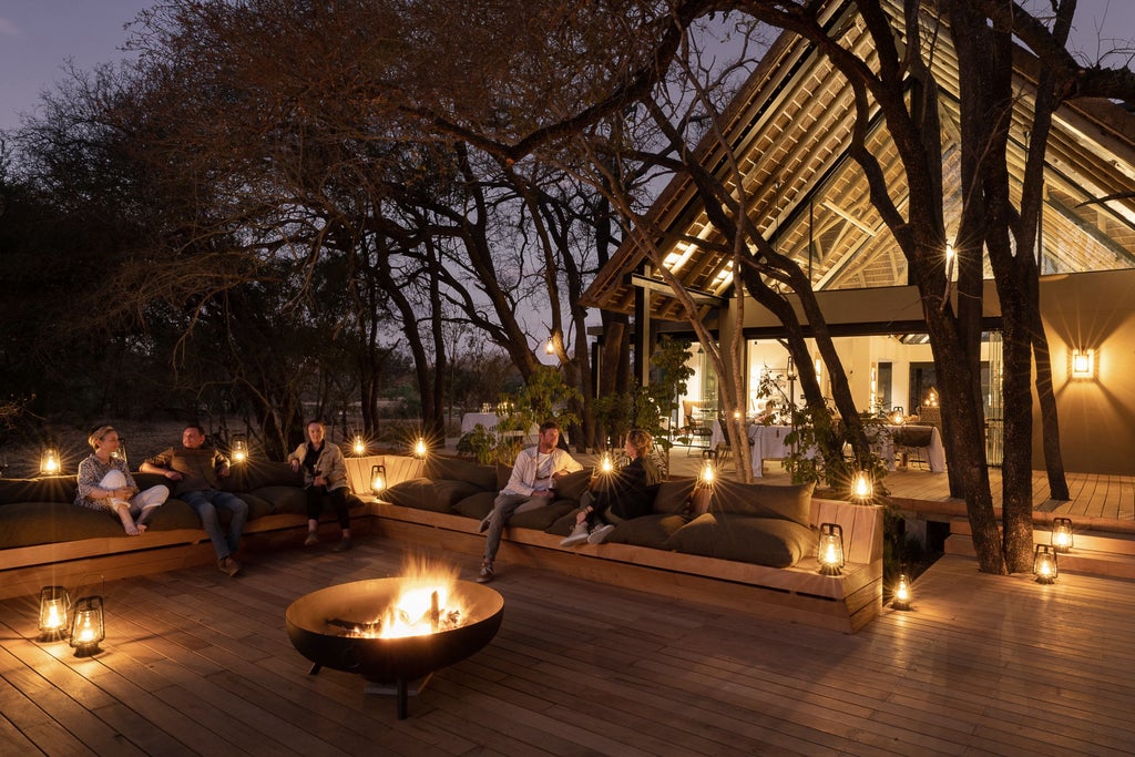 Luxurious thatched-roof safari lodge with wooden deck overlooking African savanna, private plunge pool reflecting golden sunset sky