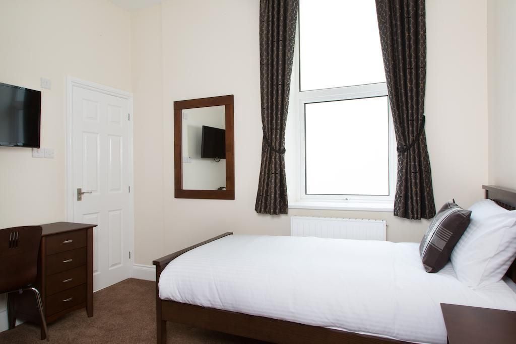 Elegant single hotel room with modern furnishings, crisp white bedding, contemporary workspace, and soft neutral color palette in UK accommodation