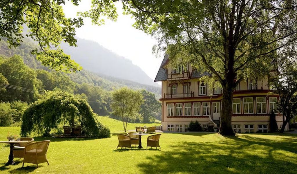 Historic Hotel Union Øye nestled against snow-capped Norwegian mountains, featuring white wooden architecture and ornate Victorian details