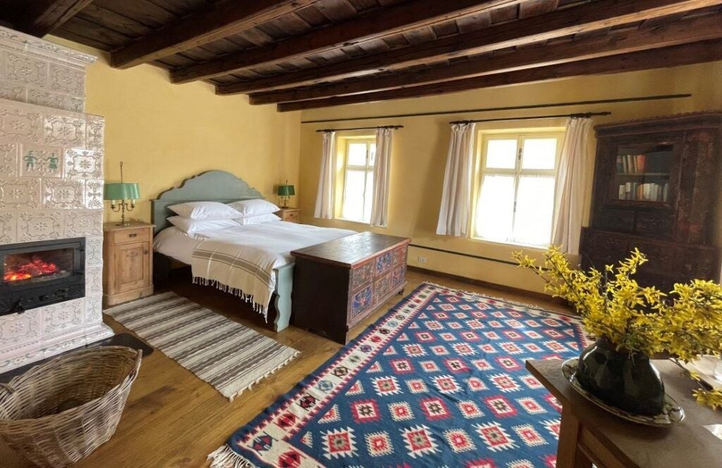 Sunlit, spacious yellow-themed suite with elegant wooden furniture, plush white bedding, and large windows overlooking Romanian countryside landscape