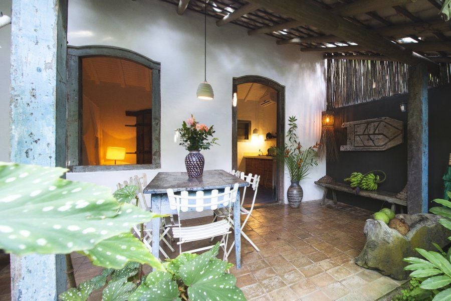 Rustic wooden four-poster bed in sunlit Brazilian eco-chic suite at UXUA Casa Hotel, featuring traditional Trancoso architectural elements and tropical decor