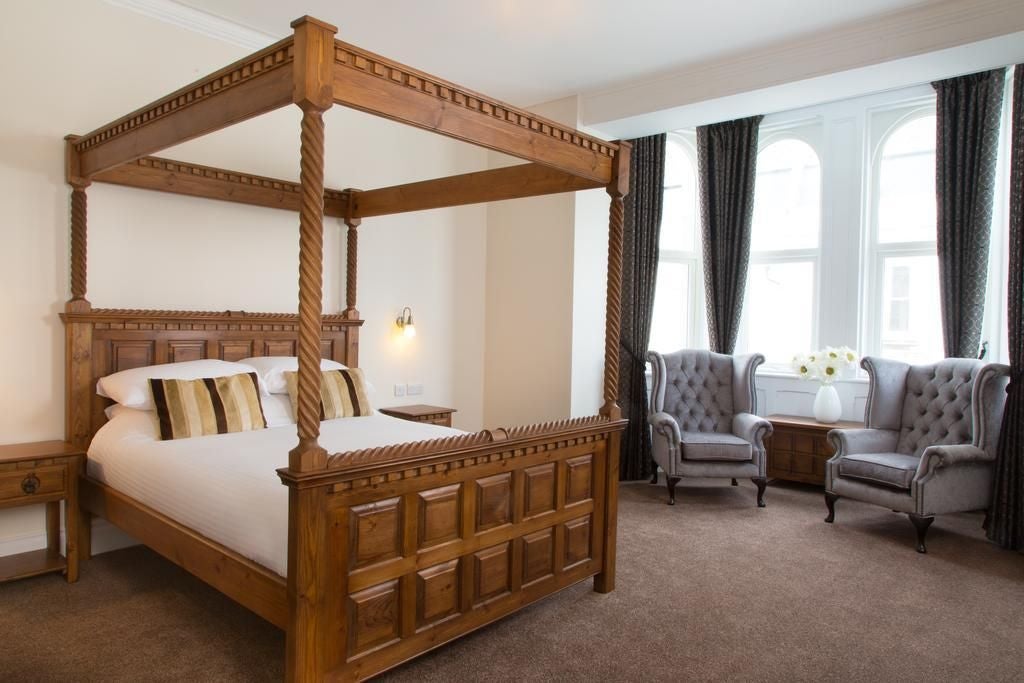 Elegant grand suite with plush king bed, rich wooden furnishings, soft neutral color palette, ornate ceiling details in historic UK hotel room