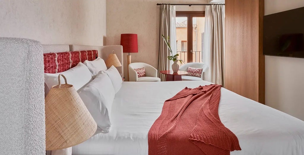 Elegant standard room with warm wooden floors, white linens, rustic Spanish-style decor, and large window overlooking charming architectural details in Posada Terra Santa.