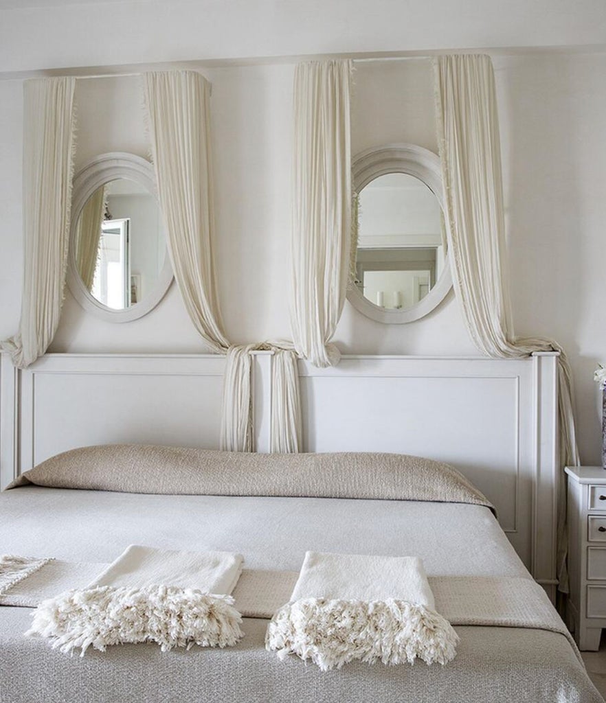 Elegant Mediterranean hotel room with stone walls, arched ceiling, and plush white bedding, featuring rustic-chic decor and soft lighting