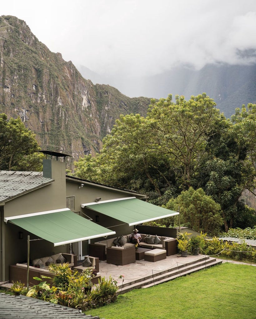 Luxurious stone facade of Sanctuary Lodge hotel nestled against misty Peruvian mountains, featuring lush garden and elegant entranceway