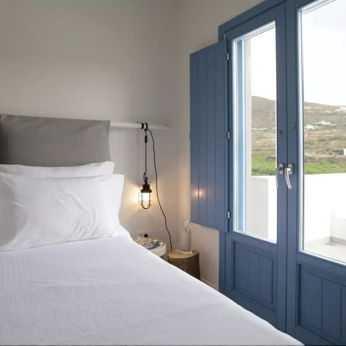 Luxurious Greek villa bedroom with elegant white-washed walls, traditional archways, and a stunning Aegean Sea view through large windows.