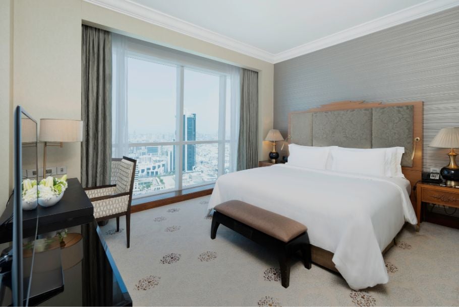 Spacious junior suite at luxury hotel with modern furnishings, plush king bed, floor-to-ceiling windows, and panoramic cityscape view in Abu Dhabi