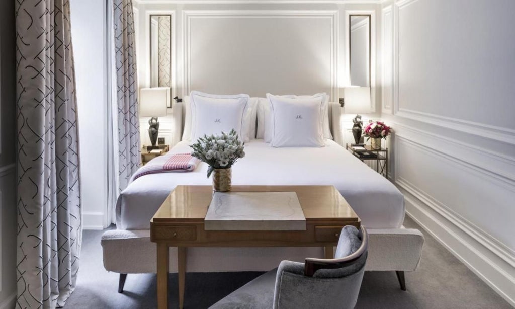 Elegant Parisian hotel room with soft neutral tones, plush white bedding, designer furnishings, and large window overlooking charming French architecture