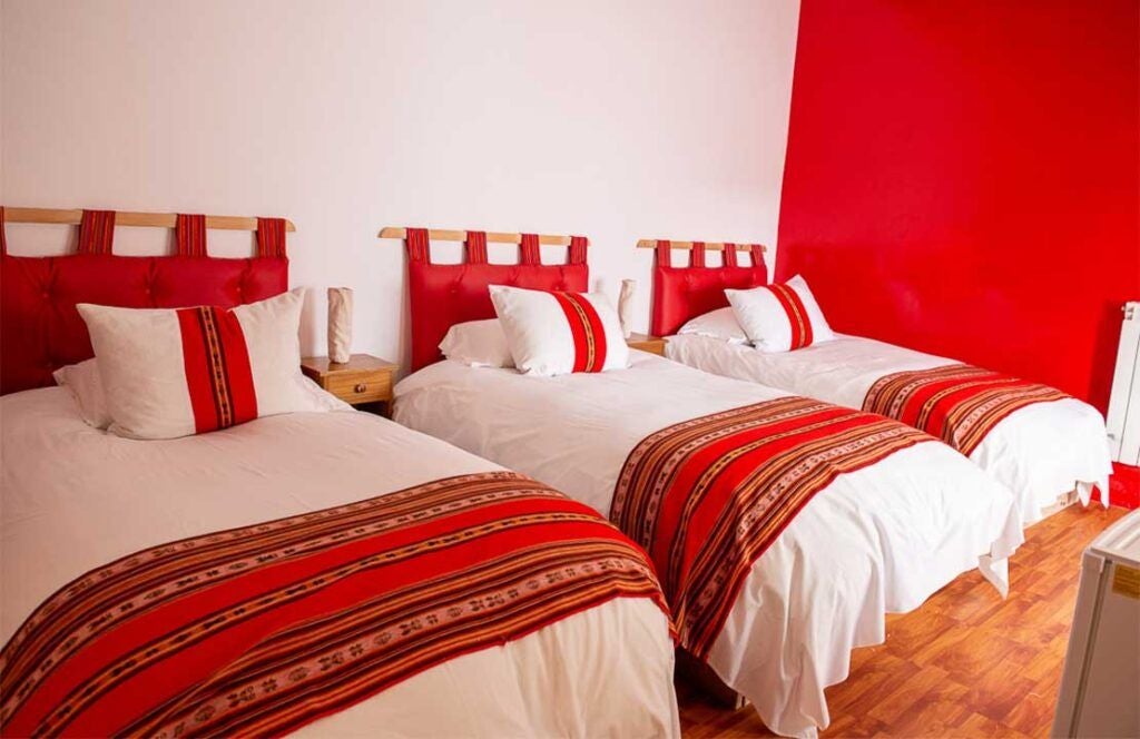 Elegant superior matrimonial hotel room with warm earth tones, traditional Bolivian textiles, and panoramic mountain landscape through large window