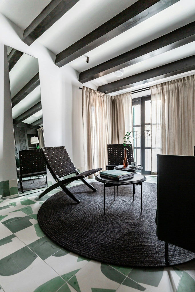 Elegant modern junior suite with minimalist design, soft neutral tones, plush white bedding, and sleek wooden furniture in contemporary Spanish hotel room