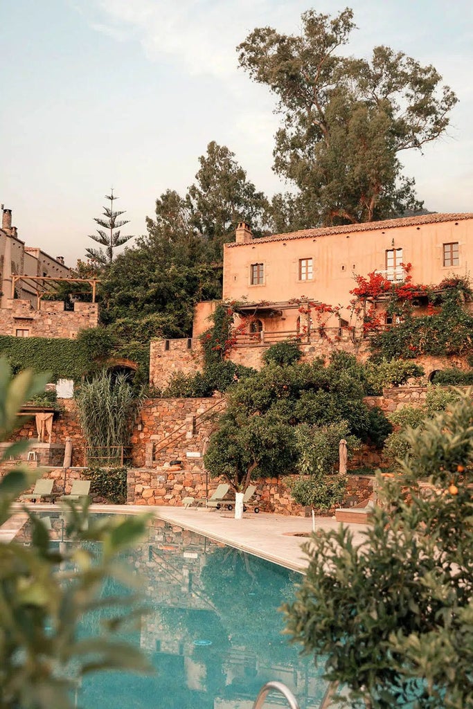 Historic stone-built luxury hotel nestled in Greek hillside with infinity pool overlooking Mediterranean Sea and lush gardens