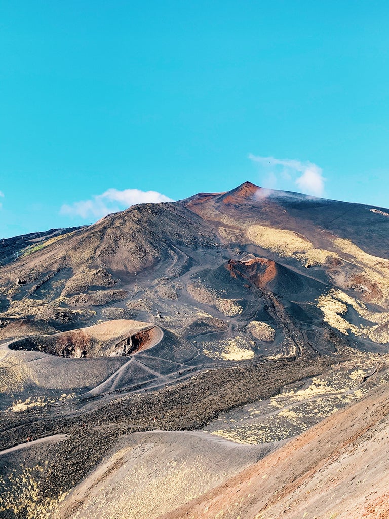 Red off-road vehicle ascending Mount Etna's volcanic landscape, with rugged black lava formations and steam vents visible in background