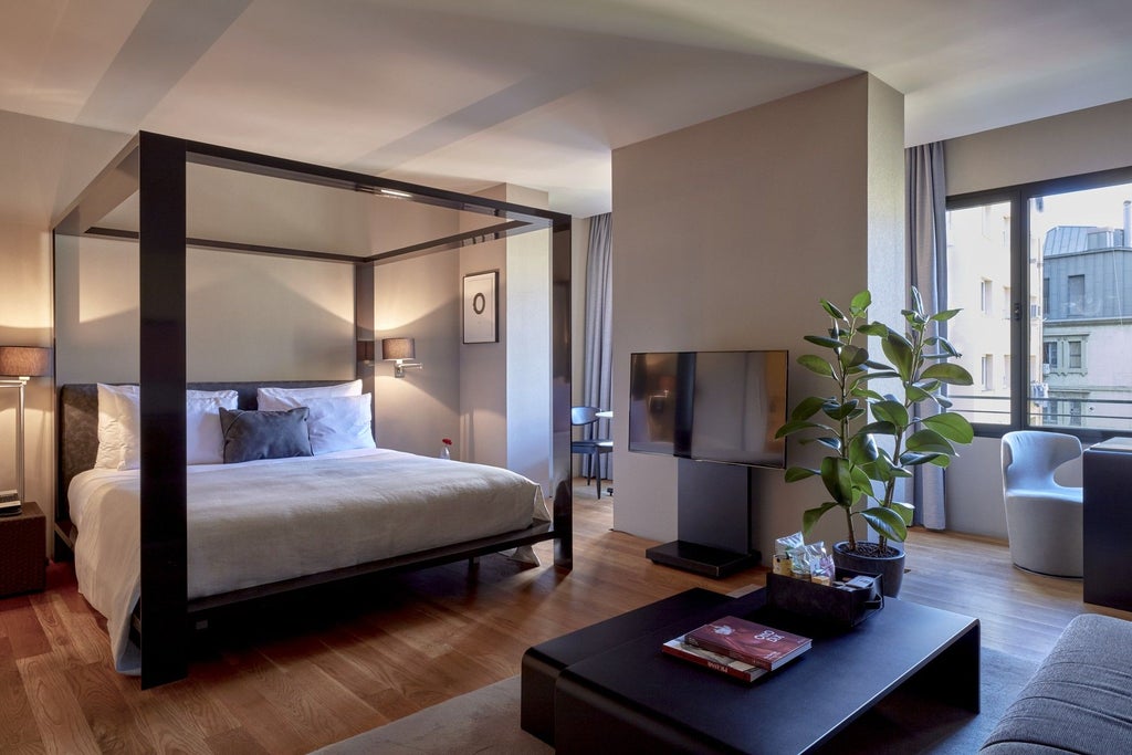 Luxurious modern hotel room with minimalist design, sleek wooden furniture, white bedding, and floor-to-ceiling windows overlooking urban Spanish landscape