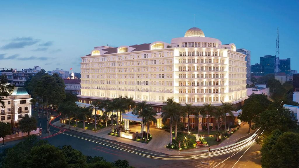 Opulent colonial-style Park Hyatt Saigon hotel facade with grand entrance, manicured palm trees and elegant French windows at dusk