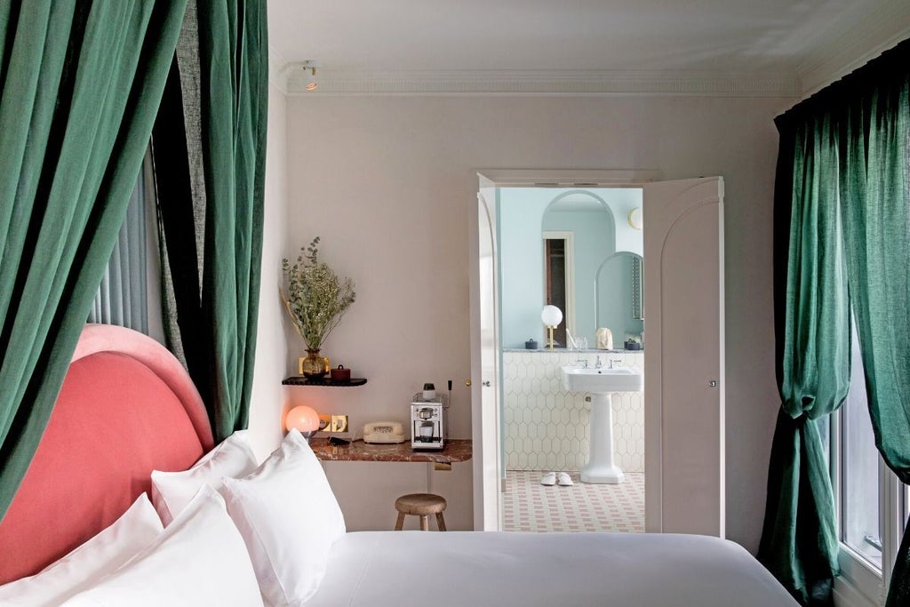 Elegant Parisian hotel room with soft neutral tones, ornate crown molding, vintage-inspired brass bed frame, and large arched windows overlooking bustling boulevard