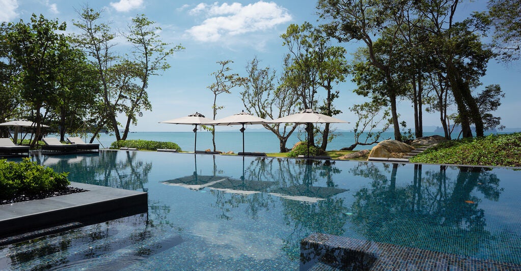 Luxurious infinity pool overlooking the Andaman Sea at sunset, with private cabanas and tropical foliage framing the panoramic view