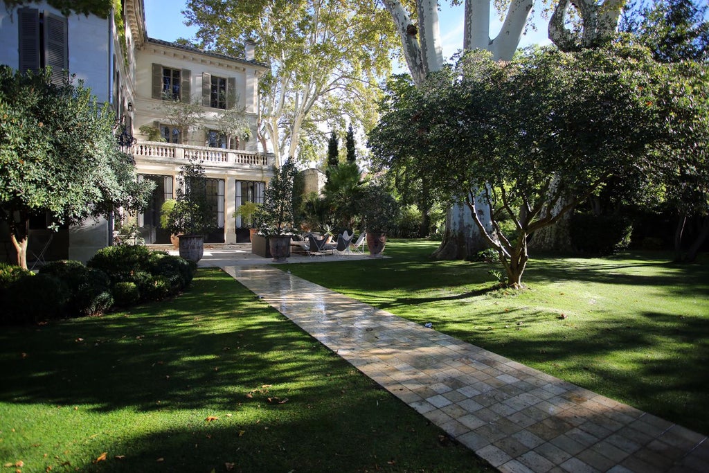 Elegant French boutique hotel facade with ornate white architecture, wrought-iron balconies, and lush green courtyard in soft afternoon light