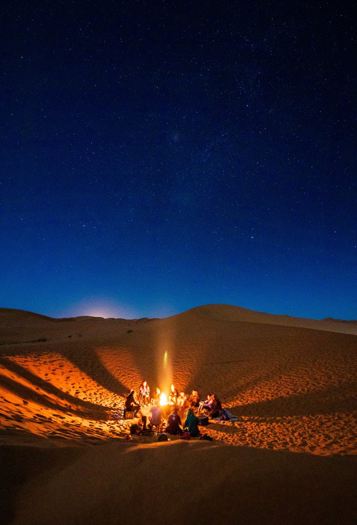 Traditional Moroccan luxury tent with ornate rugs and lanterns under starlit desert sky, golden sand dunes in background at dusk