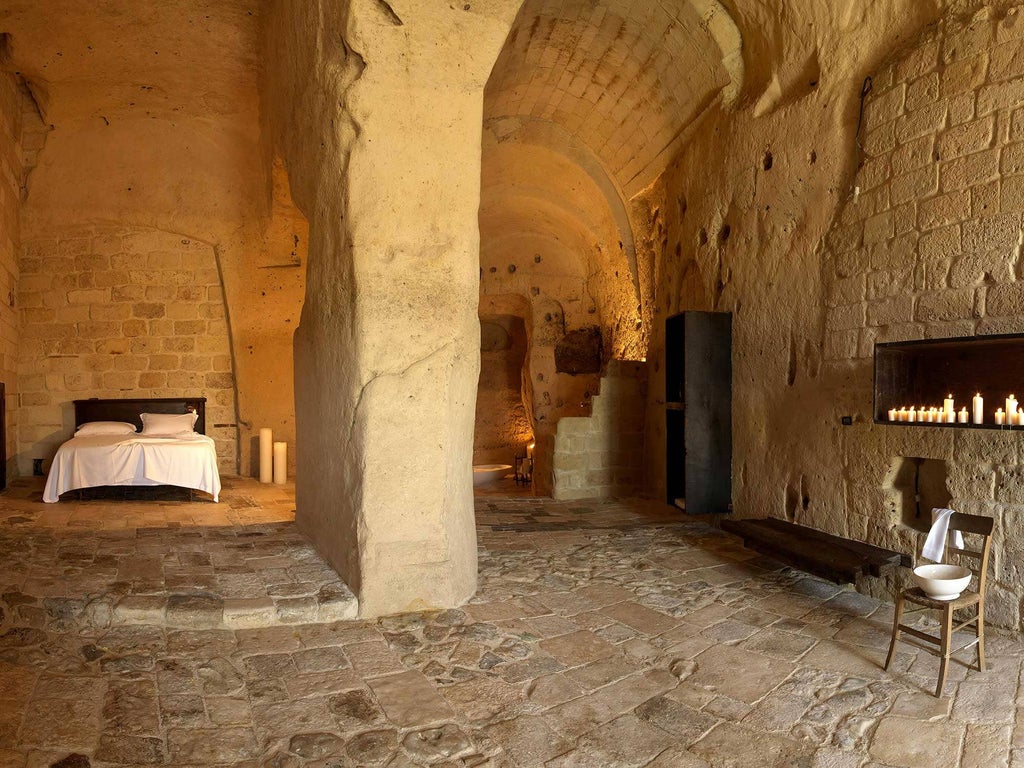 Candlelit stone cave suite with arched ceiling, rustic designer furniture, and freestanding bathtub in historic Italian hotel