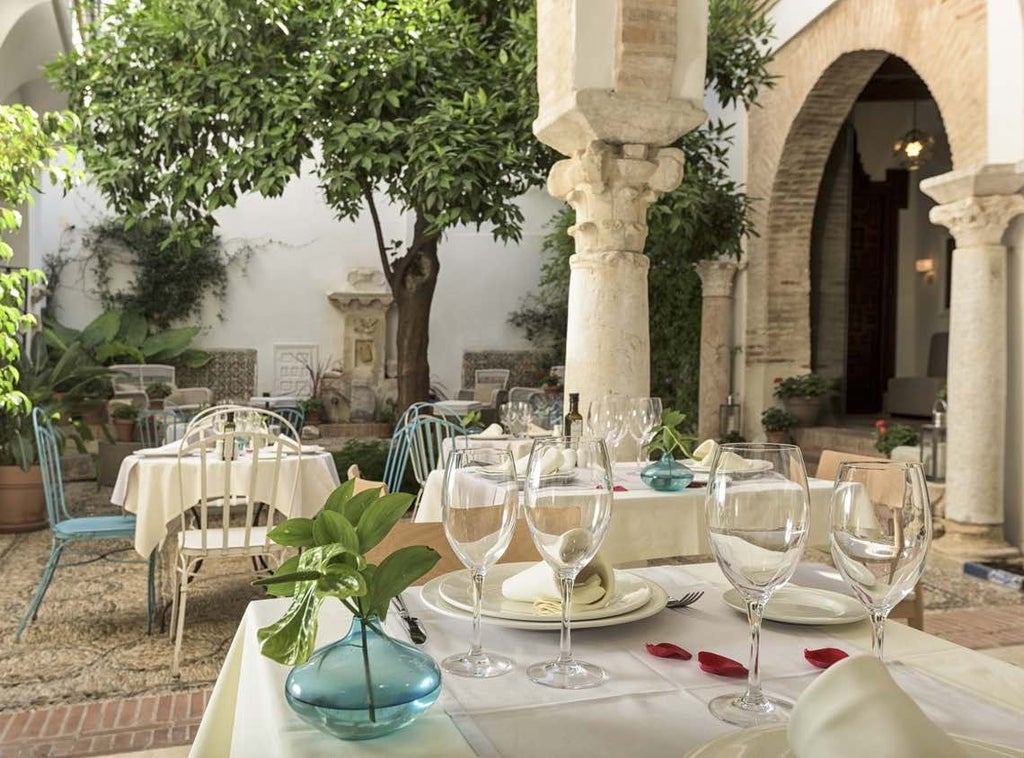 Historic Spanish colonial-style hotel with white-washed walls, arched windows, elegant balconies overlooking cobblestone streets in Córdoba's old town at golden hour