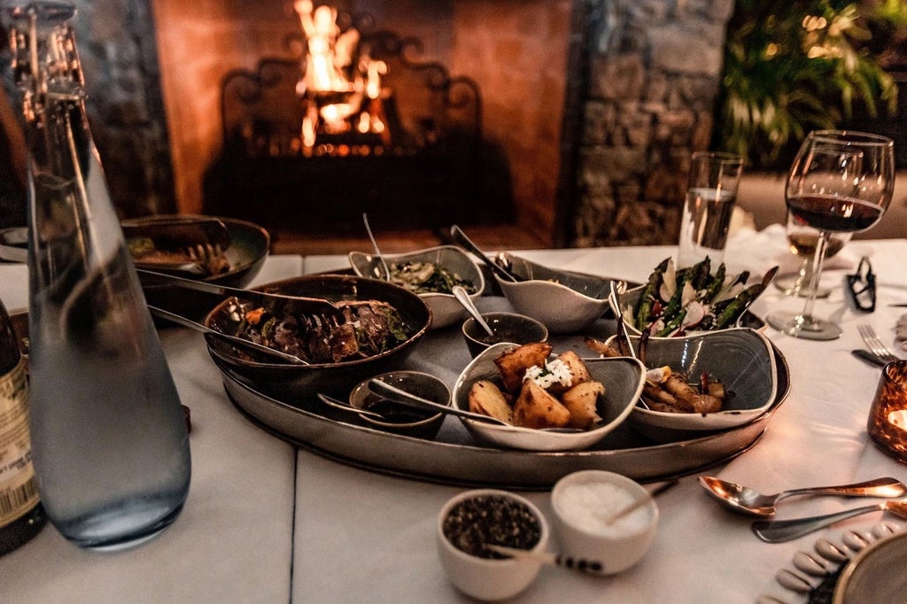 Elegant safari lodge with thatched roof and wooden deck overlooking a tranquil watering hole in the African bush at golden hour