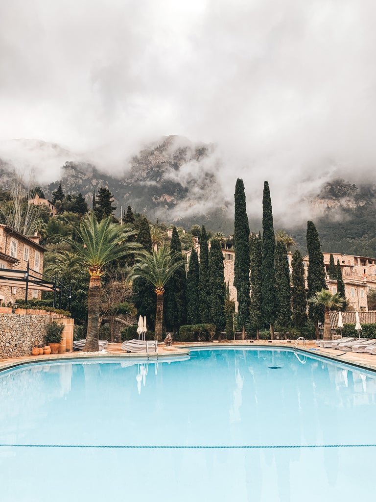 Elegant Mediterranean villa with stone facade nestled in Mallorca mountains, featuring landscaped gardens and turquoise swimming pool