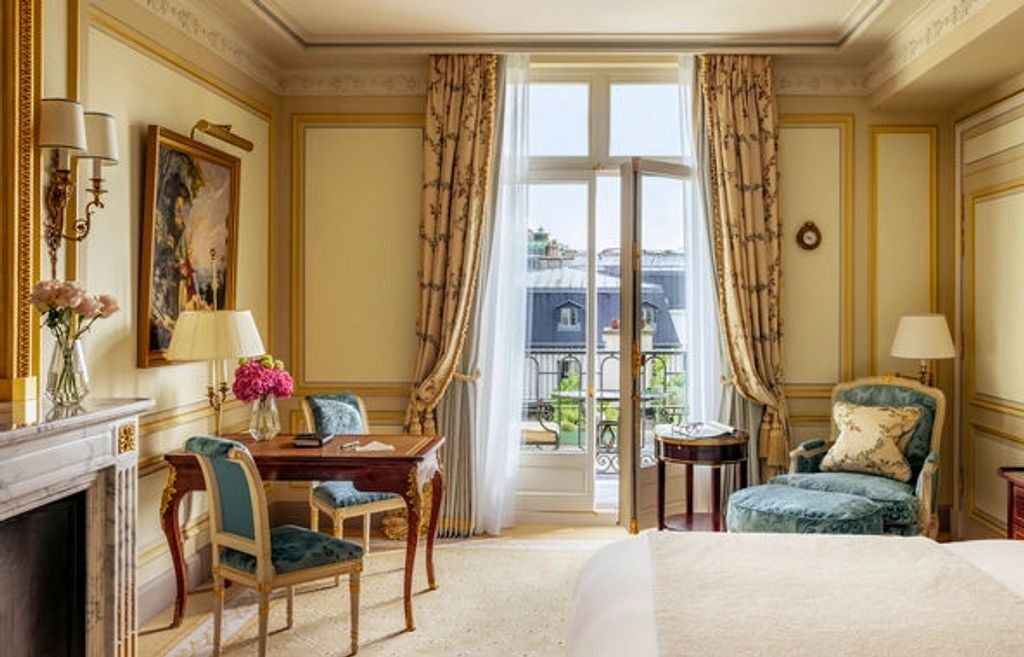 Elegant hotel room with crystal chandelier, silk drapes, marble fireplace and antique Louis XVI furniture in warm cream and gold tones