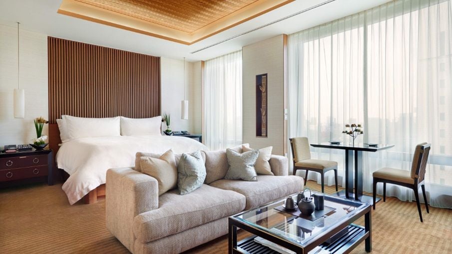 Elegant deluxe hotel room with panoramic city view, contemporary Japanese design, king bed, plush white linens, and minimalist urban sophistication at The Peninsula Tokyo