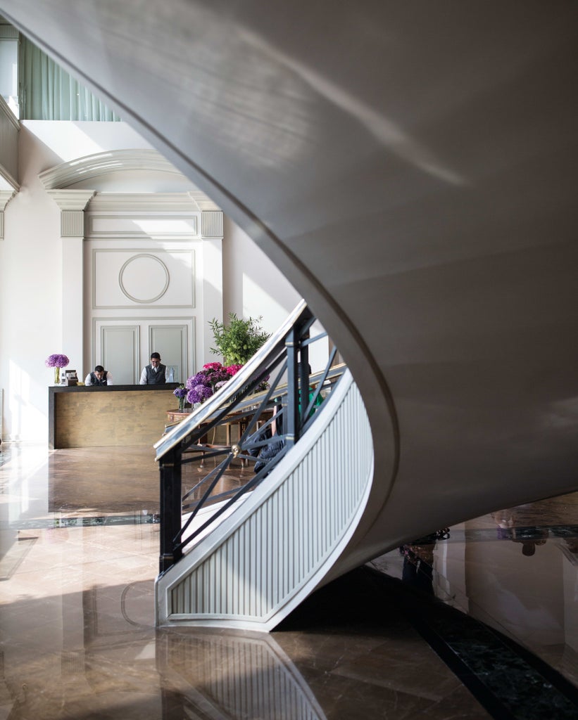 Modern beachfront luxury hotel with glass facade overlooking Lima's Pacific coast, surrounded by manicured gardens and palm trees