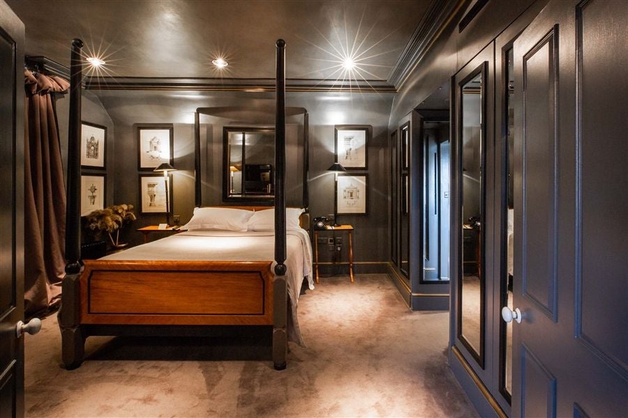 Elegant townhouse suite with dark, opulent decor, featuring plush bed, rich wood furnishings, and sophisticated lighting in a luxurious London hotel room