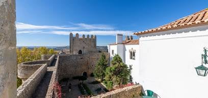 Medieval stone castle hotel with elegant turrets and arched windows perched atop a hilltop, surrounded by lush gardens in Obidos, Portugal