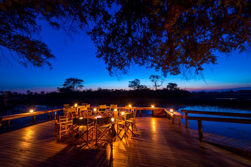 Elevated luxury safari lodge overlooking African savannah with wooden deck, plunge pool and canvas tents amid acacia trees