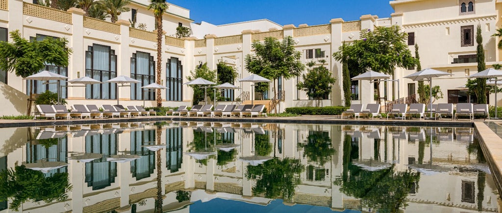 Luxurious hilltop palace hotel in Tangier with Moorish architecture, infinity pool overlooking city skyline and Mediterranean Sea at sunset