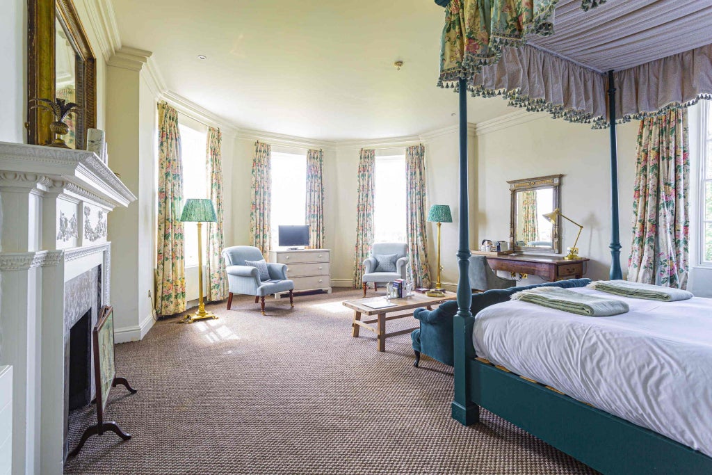 Elegant four-poster bed in luxurious cream and blue deluxe room, featuring ornate wooden furniture and soft ambient lighting at historic Talbot Hotel in UK.